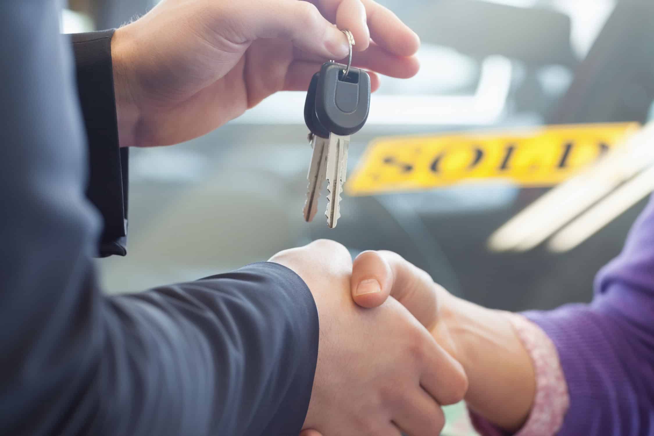 Person shaking hands in front of a sold car